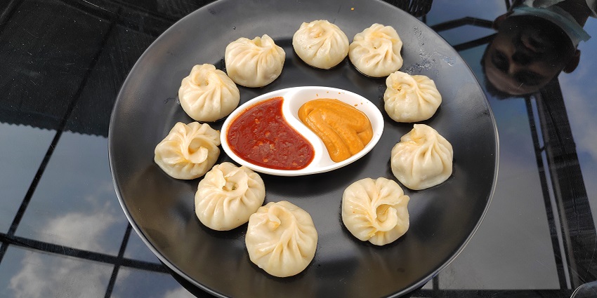 Image of chicken momo with chutney on the side served on a black plate