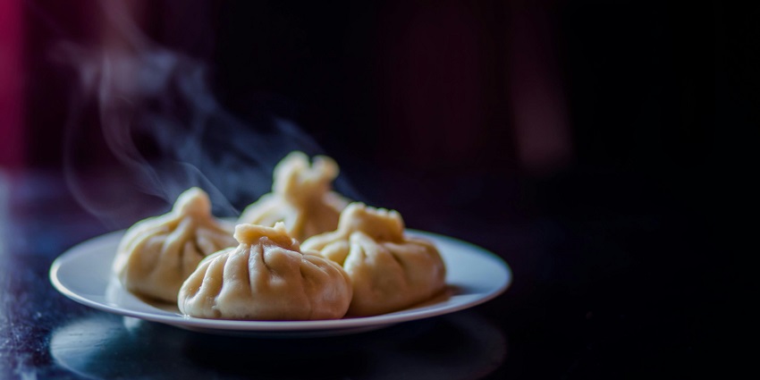 A mouth-watering view of a ceramic plate served with white dim sums sitting on a table.