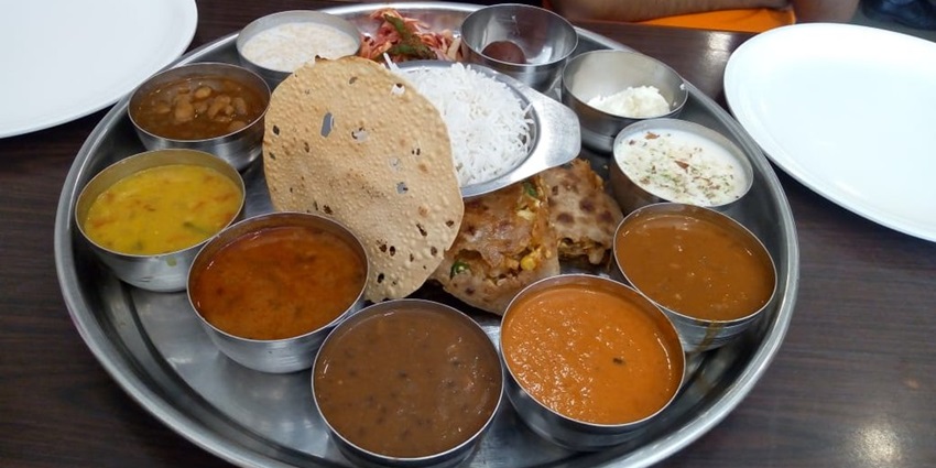 A traditional Maharashtrian thali with various dishes served on a steel plate at a restaurant