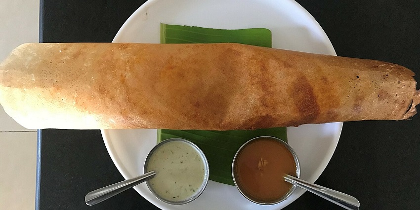 A Masala Dosa with Chutney and Sambar served on a small banana leaf in a restaurant.