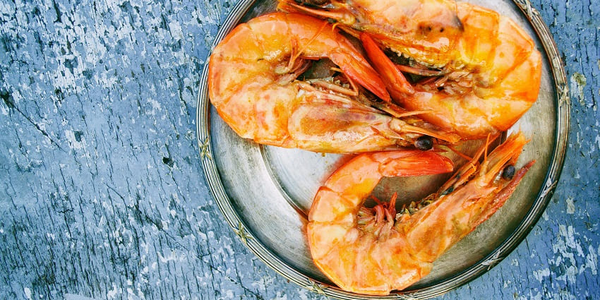 A mouthwatering view of a ceramic plate served with three cooked shrimps on a table.