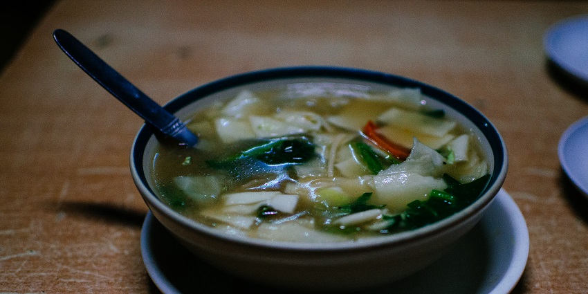 A mouth-watering view of a ceramic bowl served with Thupka and a spoon on the side.