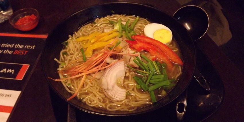 A mouth-watering view of bowl served with delicious noodle soup with a spoon on side.
