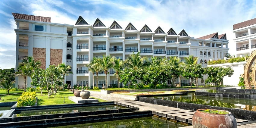 Luxurious hotel surrounded by greenery in an exotic resort setting under a clear blue sky.