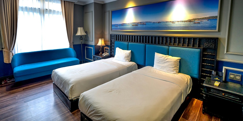 Cozy hotel room with two beds, nightstand, and large window letting in natural light