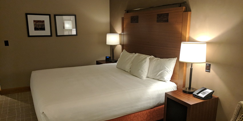 Image of a hotel room with clean bed sheets, bed, chair, table and lamps for travel accommodation