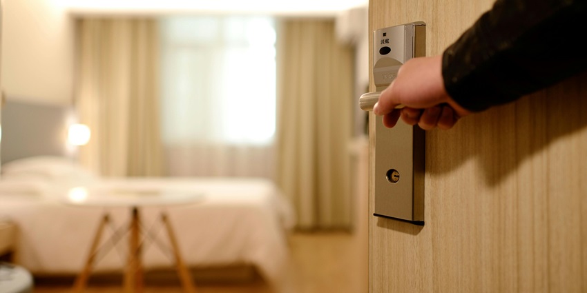 A representative image of a person holding a door lever inside a room in a hotel.