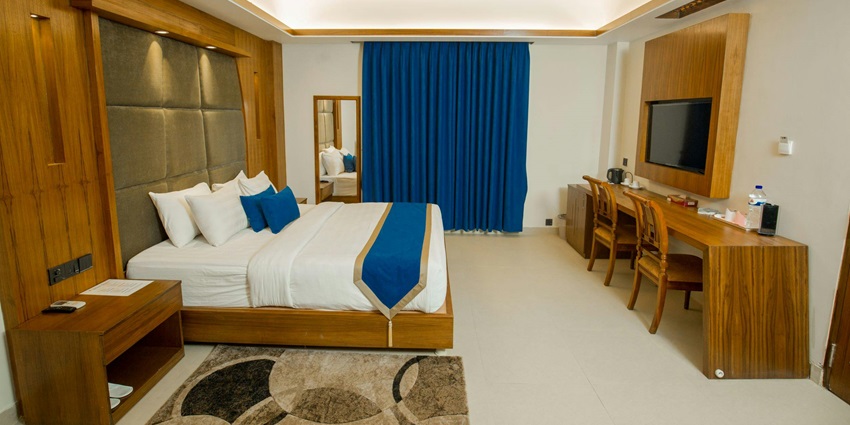 Hotel room interior with a double bed, desk, and large windows at a hotel.