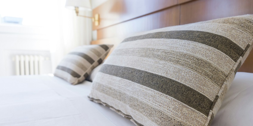 An image of a cosy hotel room with grey and black throw pillows neatly arranged on a bed.