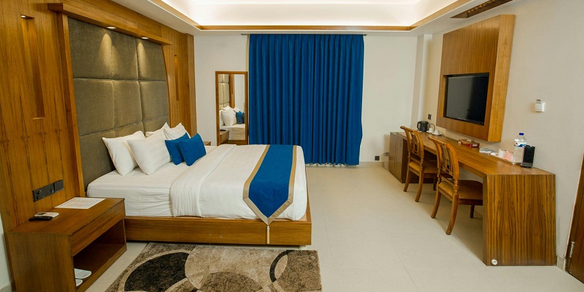 View of a hotel room featuring a bed, table and a large window covered with curtains