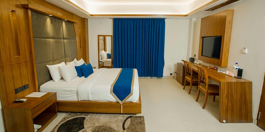 A well-lit hotel room with modern decor, featuring a double bed and large windows.