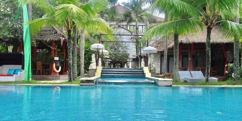 An inside view of a resort with a pool and sunbeds along with palm trees on the side