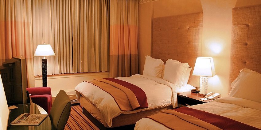 Image of a hotel room with dim lights bed, clean sheets and pillows also sofa on the side