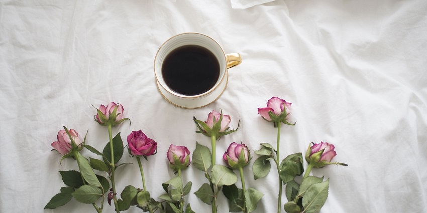 A cosy bed with a tray of coffee and fresh roses, creating a relaxing morning atmosphere.
