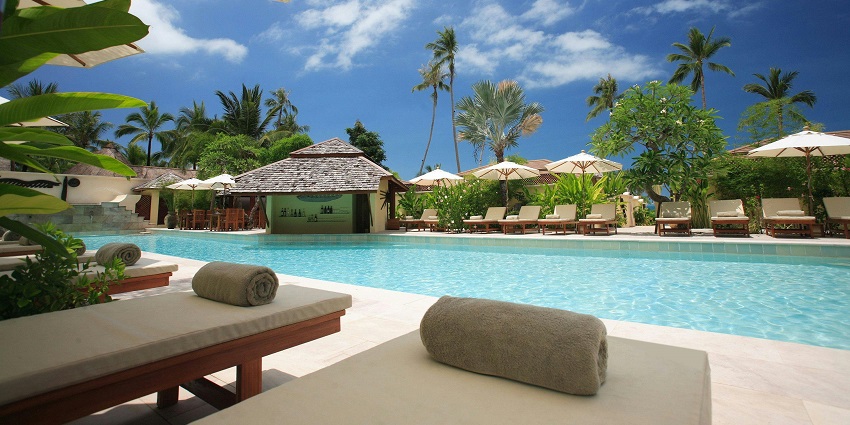 A picture of a tropical resort surrounded by lush greenery, with a pool in the foreground.