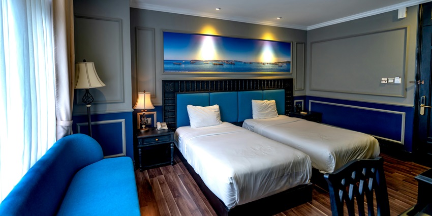 A hotel room with beautiful blue furniture, white bed linen, and a window view