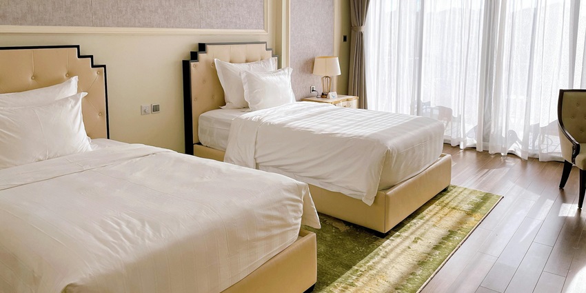 A hotel room with blue furniture, white bed linen, and a large window with sheer curtains