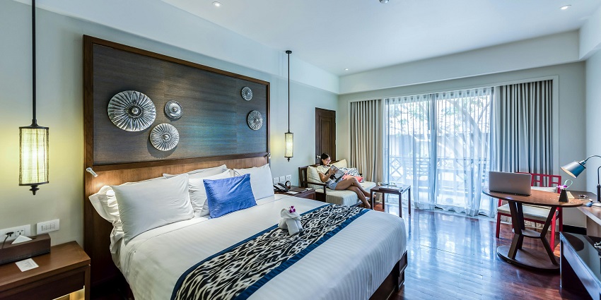 A photo of a minimalist hotel room with a white bed and grey walls near the lizard temple