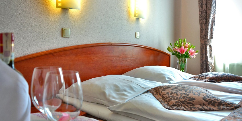 Image of a hotel room with a bed, table, chair and clear sheets and glasses on the side