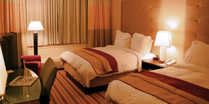 The inside of a hotel room with beautiful wooden interiors and properly made bed with dim lights.