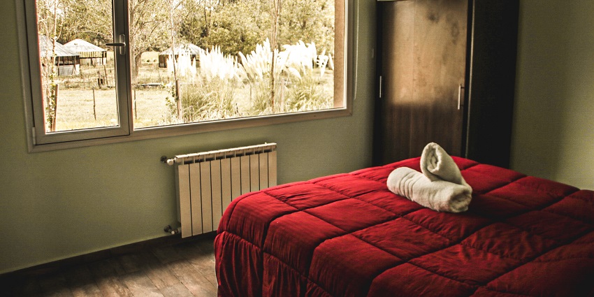 Image of a hotel room with a bed clean sheets and towels on it and a window for outside view