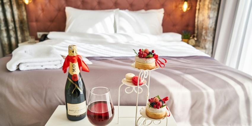Romantic setting with a wine bottle and gourmet food on a cosy hotel bedroom table.