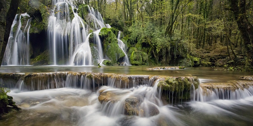 Burude Falls cascading down rocky cliffs surrounded by dense green trees.