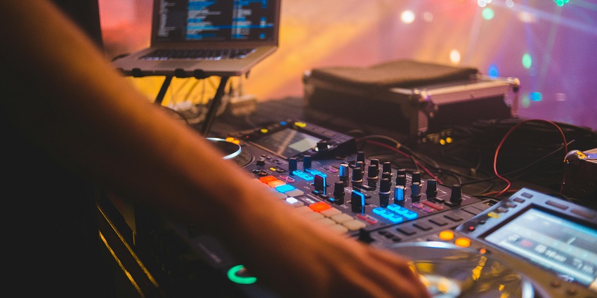 Several people dancing to the beat on the dance floor with a vibrant DJ and loud music.