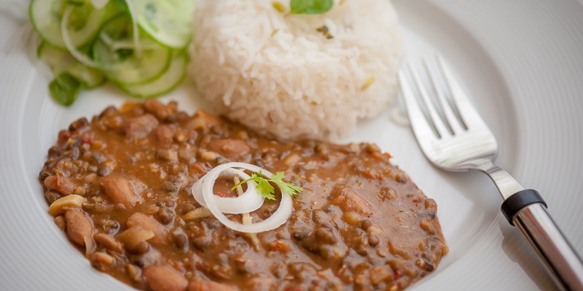 A picture of Punjabi Dal Makhani, rice, salad and onion with fork on a white plate.
