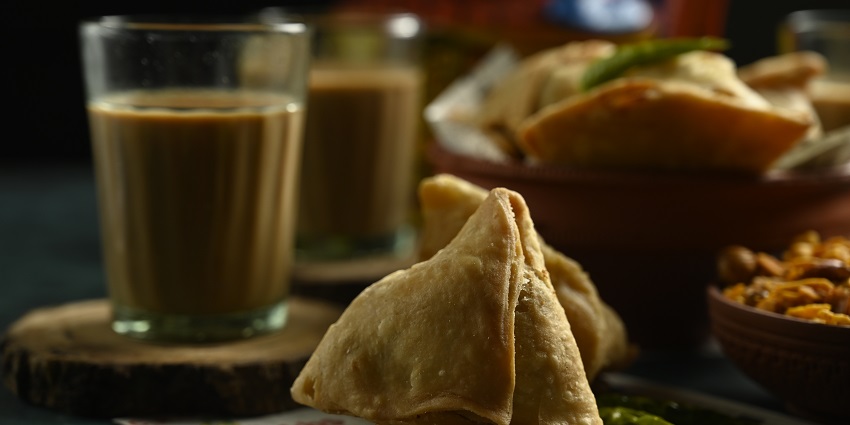 A cup of steaming hot chai served with crispy samosas