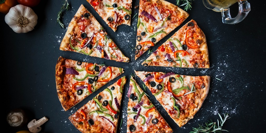 An eight-sliced pizza topped with cheese and veggies with a bite taken from one slice