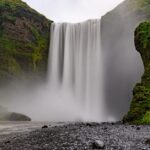 Zenith waterfall cascading down a rocky cliff into a misty river, surrounded by lush greenery