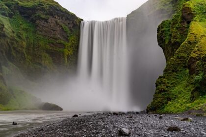 Zenith waterfall cascading down a rocky cliff into a misty river, surrounded by lush greenery