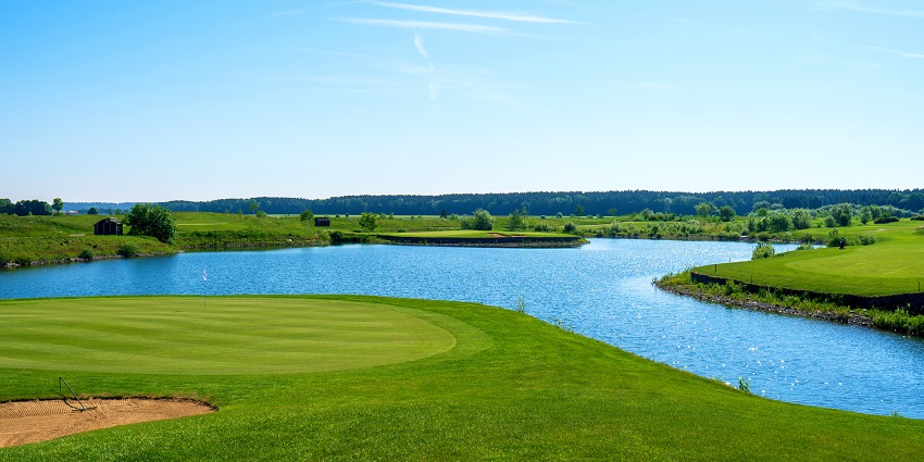 A golf course with clean cut green grass at a stretch under cloudy sky.