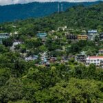 A picture of a house situated in a green hilly area right under the cloudy skies.