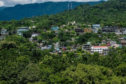 A picture of a house situated in a green hilly area right under the cloudy skies.