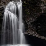 A serene waterfall in Aurangabad which flows over moss-covered rocks into a clear river, surrounded by lush green trees.