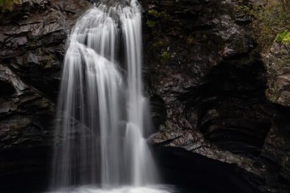 A serene waterfall in Aurangabad which flows over moss-covered rocks into a clear river, surrounded by lush green trees.