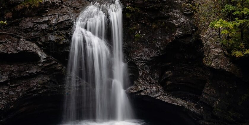 A serene waterfall in Aurangabad which flows over moss-covered rocks into a clear river, surrounded by lush green trees.