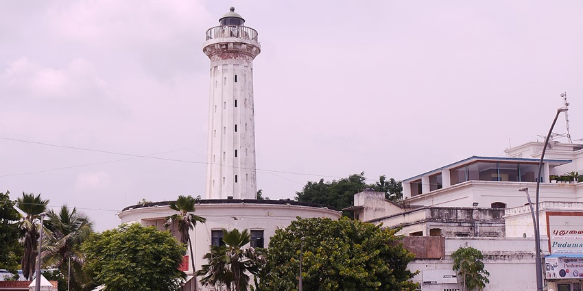 An old brick lighthouse in Pondicherry surrounded by green grass and a metal fence.