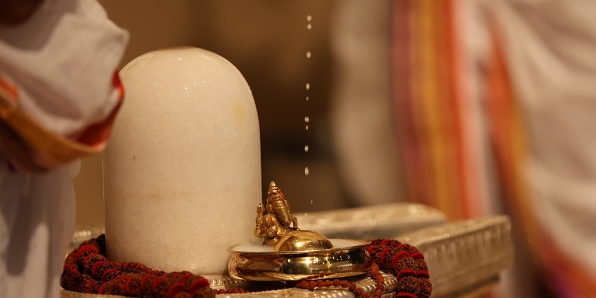A Shiva Abhishekam is being performed on the white marble Shivalinga in a temple.