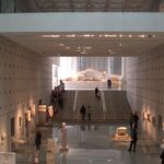 Interior of Acropolis Museum with stairs, first floor and people exploring the antiques.