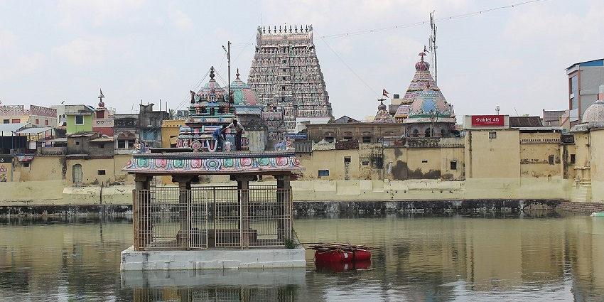 Entry structural gate of Adi Kumbeswarar temple with people standing and vehicles parked.