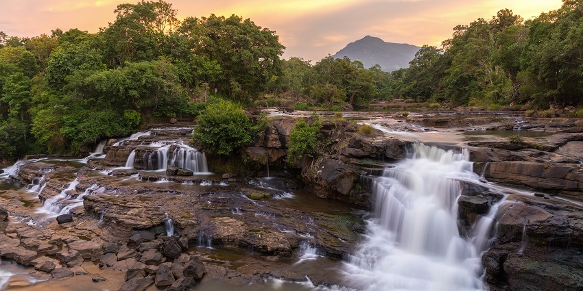 Water flows from high mountains to below them while the sun shines through the blue open sky.