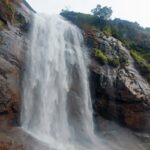 View of Aagai Gangai Falls flowing down a rocky hillside, surrounded by dense green forest