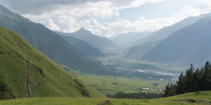 A picture of a valley with lush green mountains on both sides