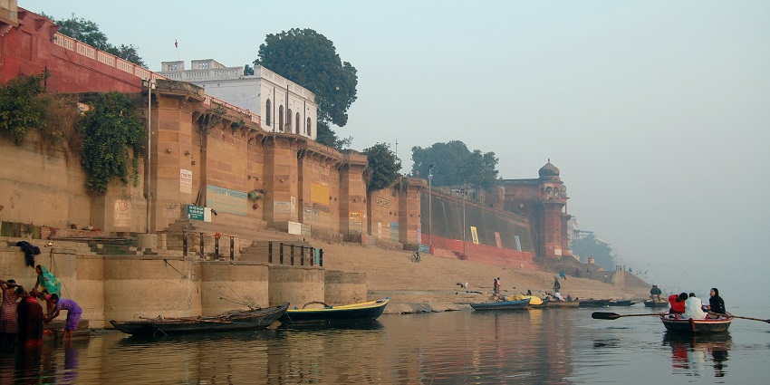 Morning view of a Ghat with few people boating and some boats standing by the steps