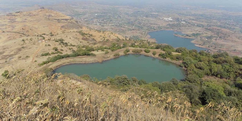 A picture of Anjaneri Lake near Nashik, surrounded by lush greenery and rolling hills.