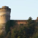 Majestic tower and castle perched on a hill, surrounded by lush greenery and a clear blue sky