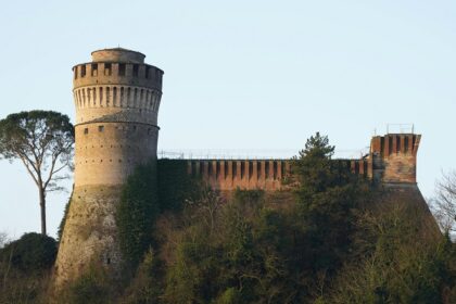 Majestic tower and castle perched on a hill, surrounded by lush greenery and a clear blue sky